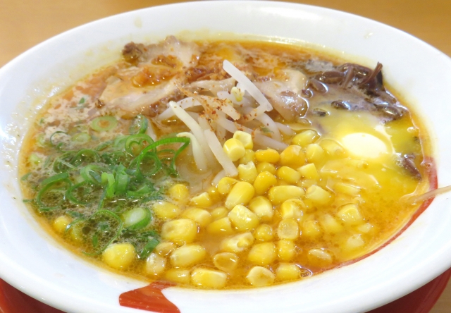 A bowl of miso ramen with a rich, savory broth, topped with corn, butter, green onions, and slices of pork