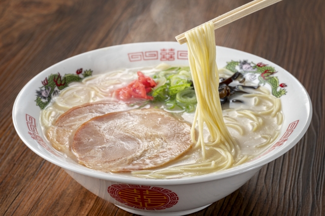 A bowl of Hakata tonkotsu ramen with a creamy pork bone broth, topped with thin noodles, chashu pork, green onions, and red pickled ginger