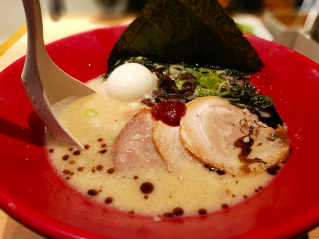 A bowl of Tonkotsu ramen featuring a rich tonkotsu broth, thin noodles, slices of pork, and a dollop of their signature spicy red sauce.