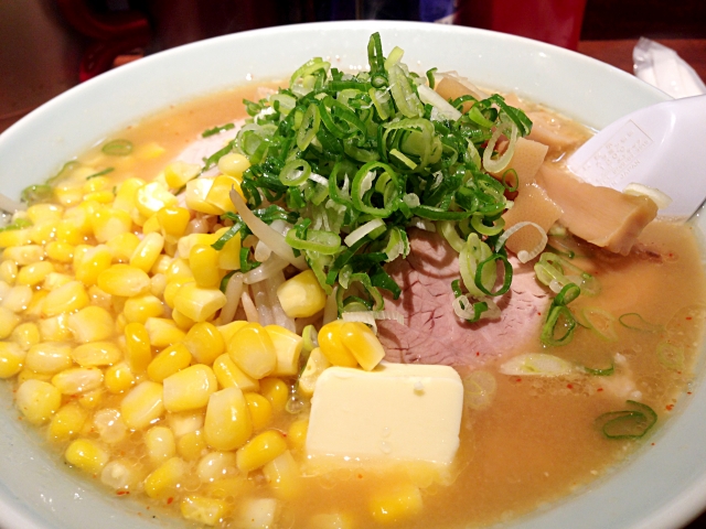 A bowl of miso ramen with a rich, savory broth, topped with corn, butter, green onions, and slices of pork