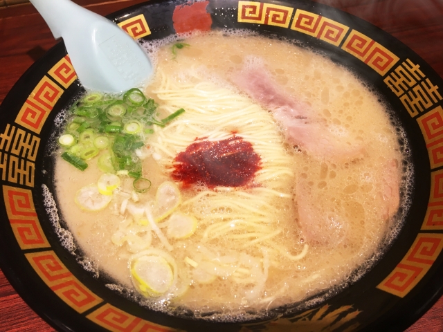 A bowl of Ichiran ramen featuring a rich tonkotsu broth, thin noodles, slices of pork, and a dollop of their signature spicy red sauce